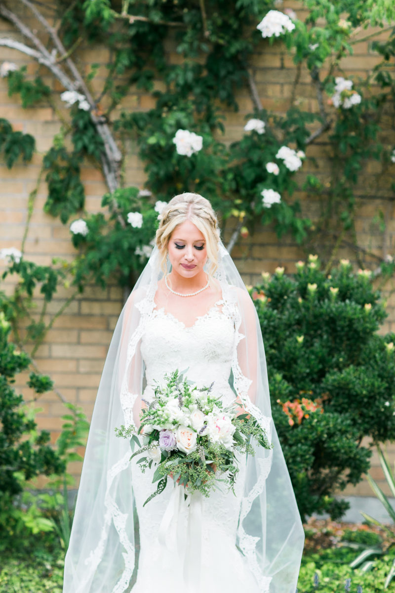 Bride looking down and lavender and white bouquet in wedding dress and long veil