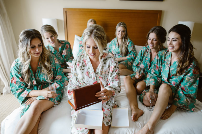Bride opening gift from Groom in front of Bridesmaids in floral getting ready robes