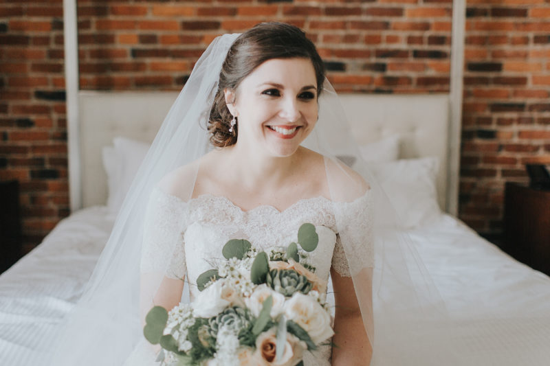 Bride with green and wide bouquet in veil and wedding dress with lace sleeves