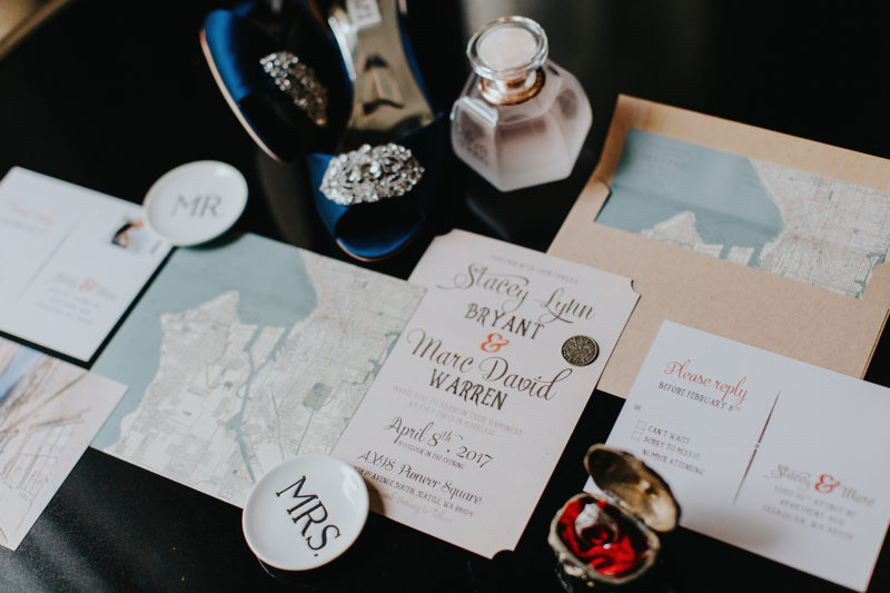 Map lined custom wedding invitation styled with wedding rings, shoes and perfume