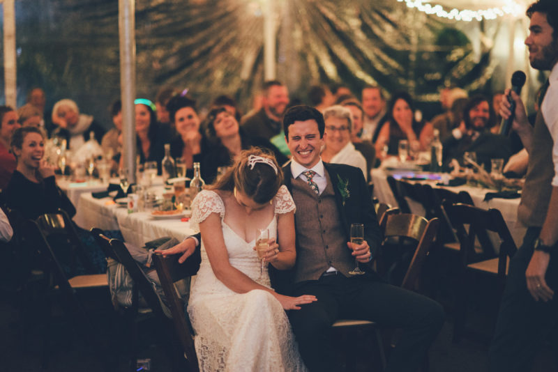 Toasts is tent with twinkle lights Bride and Groom laughing