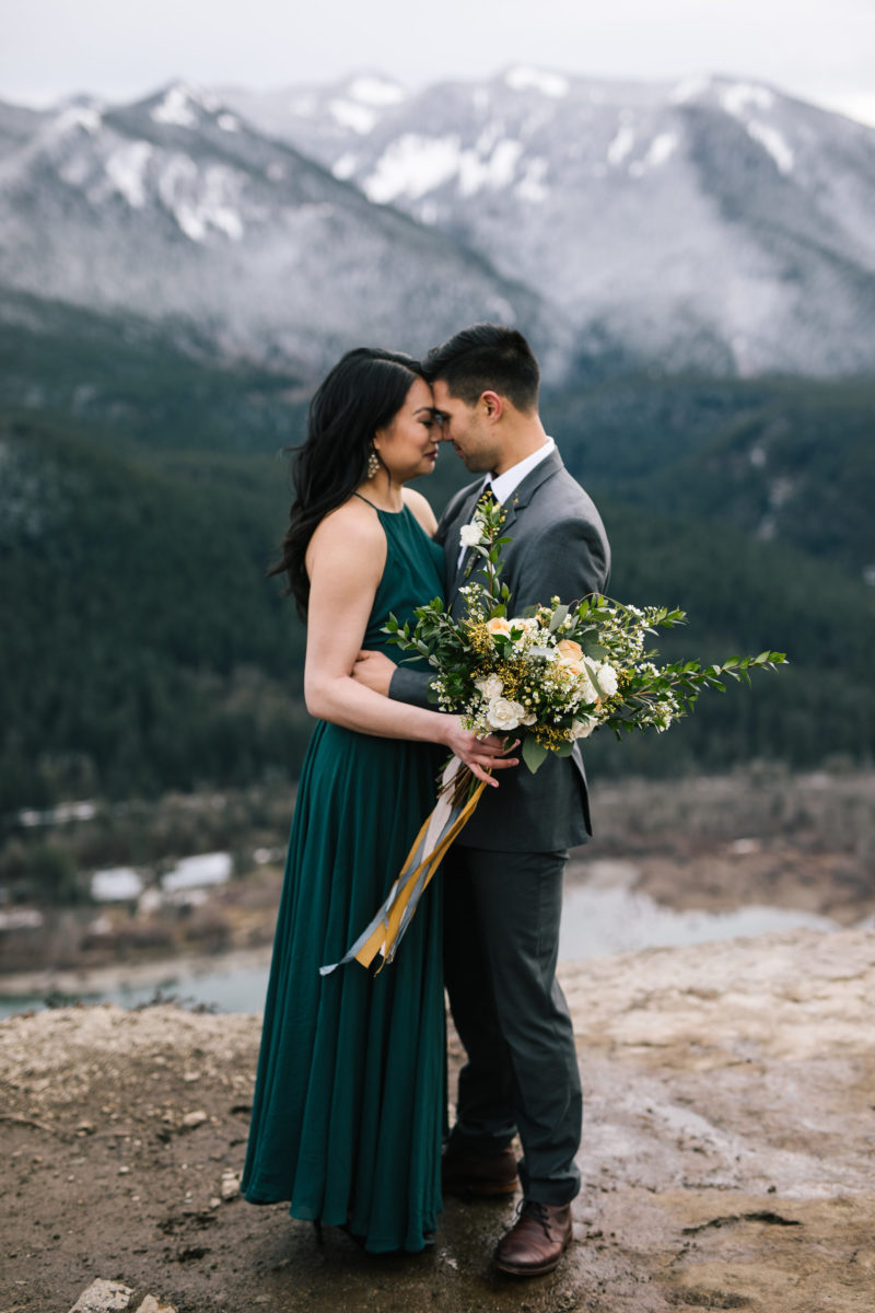 Bride and Groom on edge of Rattlesnake Ridge with yellow bridal bouquet snowy mountains in background