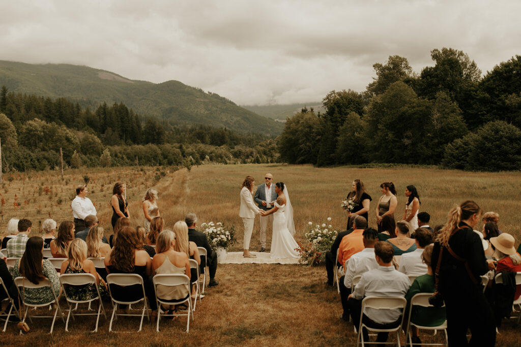 Two brides holding hands during their wedding ceremony in a meadow near Mount Baker!
